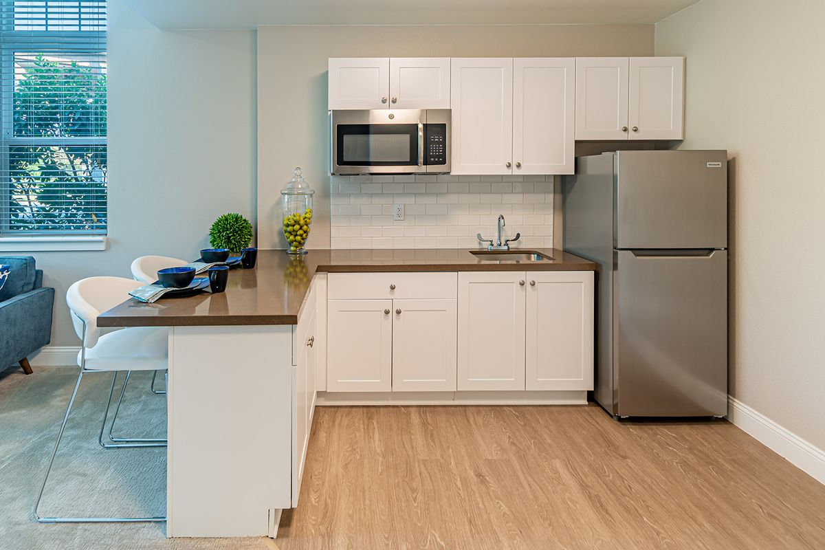 A modern kitchen with white cabinets, a stainless steel refrigerator, and a microwave.