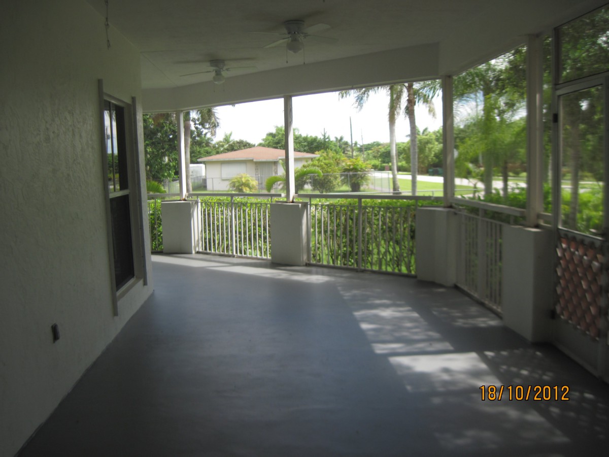 A spacious covered porch with railings, offering a view of tropical palm trees.