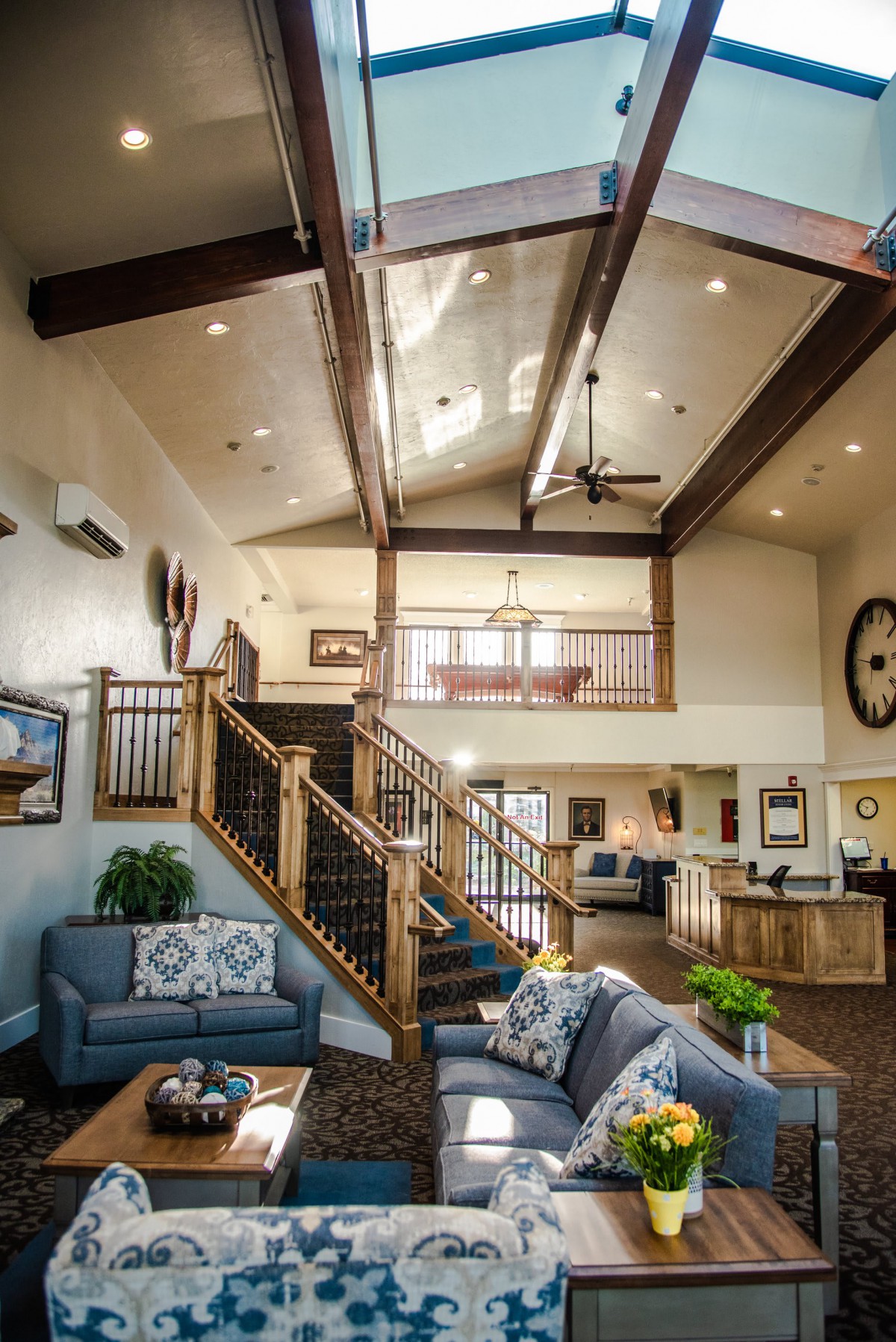 A modern living room with vaulted ceilings and wooden beams, featuring a loft area and a staircase.