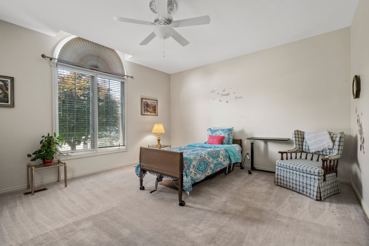 A cozy bedroom with a single bed, desk, and chair under natural light from a large window.