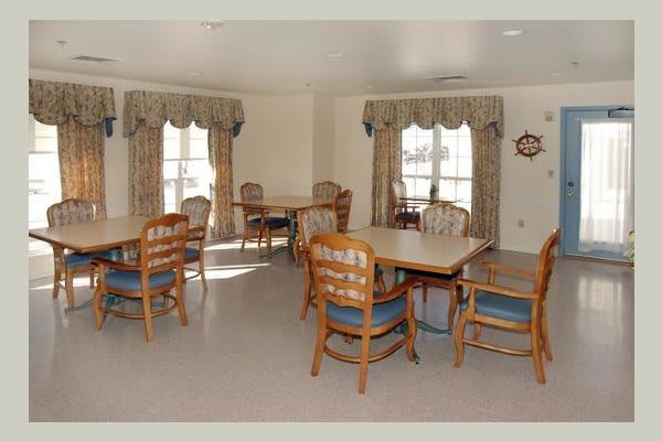 A spacious dining area with multiple tables and chairs, featuring large windows with curtains.