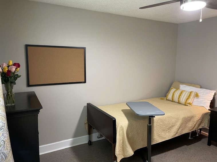 A minimalist bedroom with a bed, small desk, and an empty corkboard on the wall.