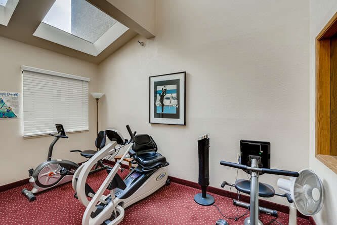 A small gym room featuring exercise bicycles and fitness equipment with a decorative artwork on the wall.