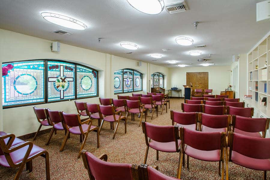 An empty room with rows of chairs and decorative stained glass windows.