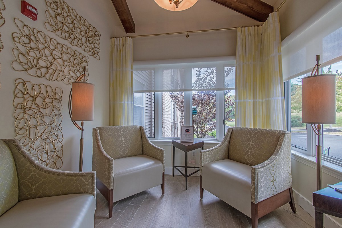 A cozy living room with neutral-colored chairs, a window with curtains, and a decorative wall.
