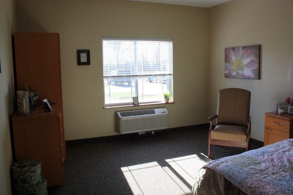 A minimalist room with a bed, chair, and a window letting in natural light.