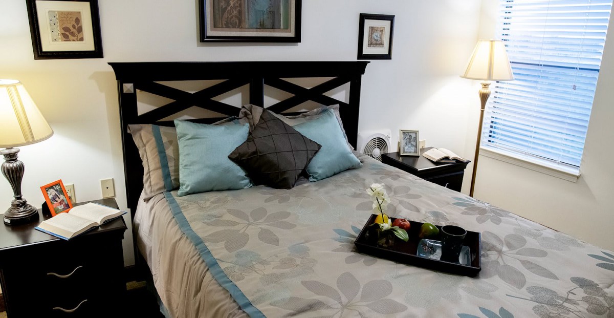A cozy bedroom with a neatly made bed, accent pillows, and decorative elements on the nightstand.