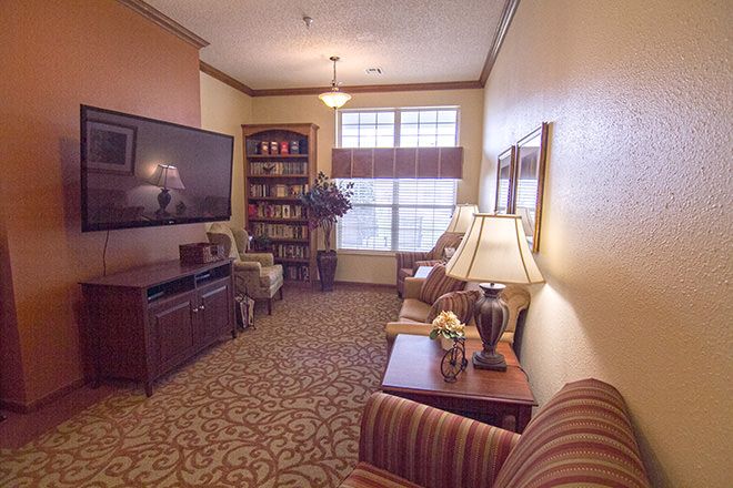 A cozy living room with comfortable seating, a large television, bookshelf, and warm lighting.
