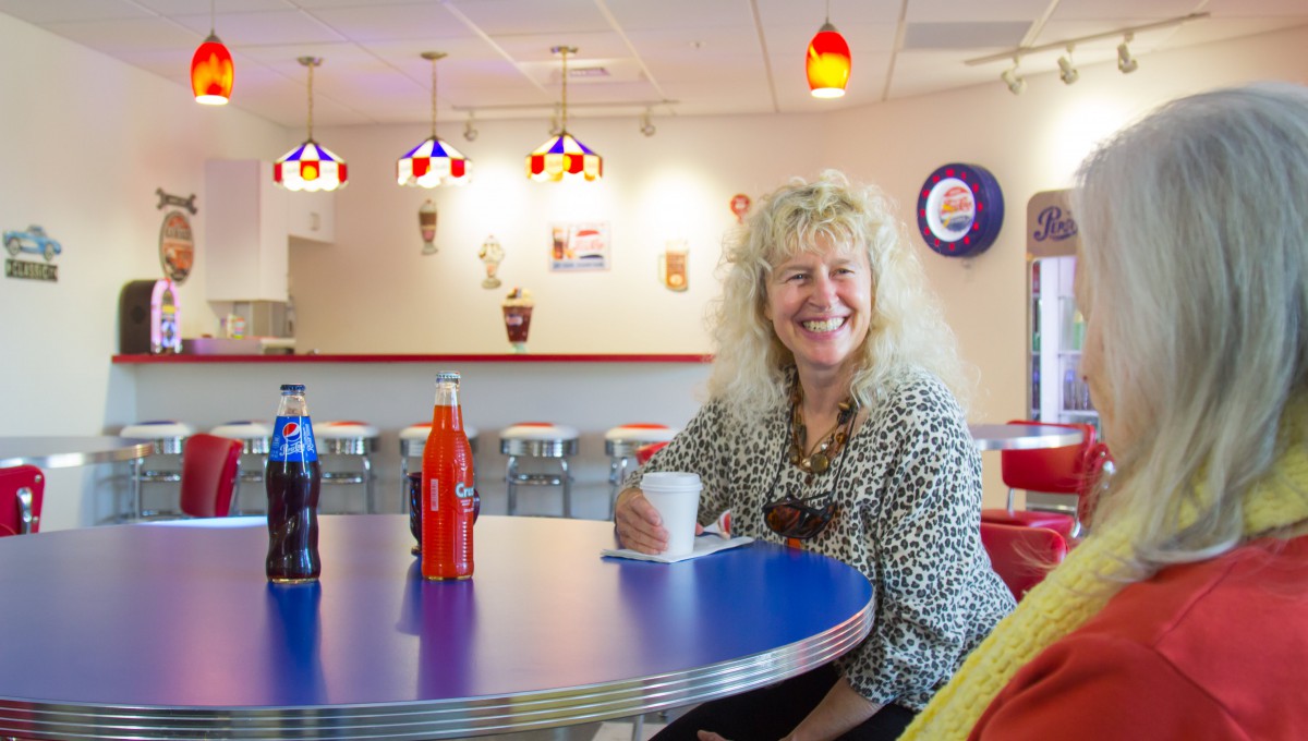 A woman smiling while holding a coffee cup in a modern, retro-style diner.