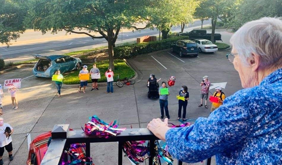 A group of people stand in a parking lot, some holding signs and balloons, viewed from a balcony.