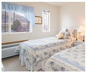 A cozy bedroom with two twin beds covered in floral bedding, featuring a large window with blue curtains.