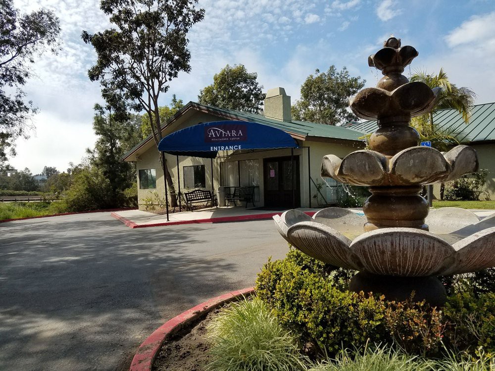 A scenic view of a building entrance with a fountain in the foreground and trees surrounding the area.
