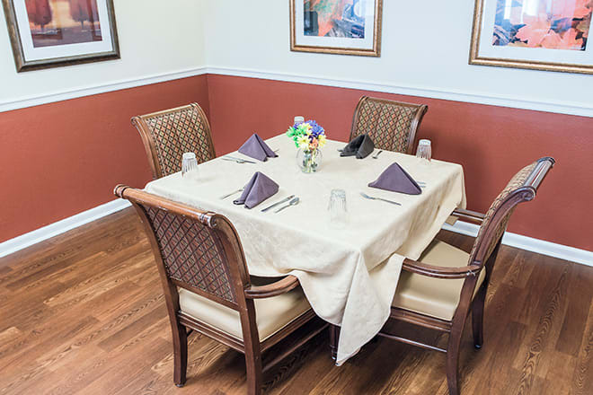A neatly set dining table with four chairs in a restaurant, featuring elegant napkins and a floral centerpiece.