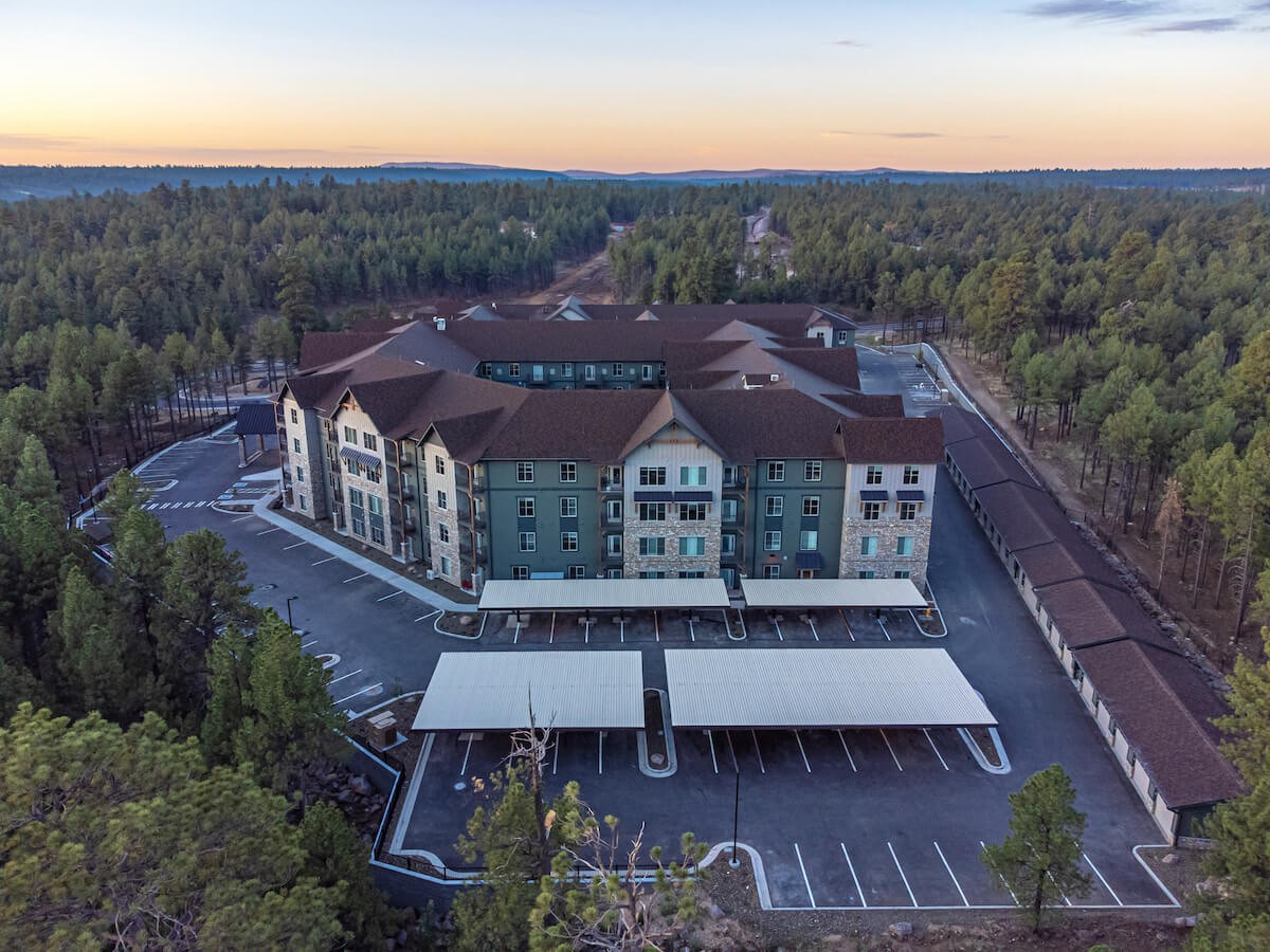 Aerial view of a resort surrounded by a forest during sunset, featuring a spacious parking area.