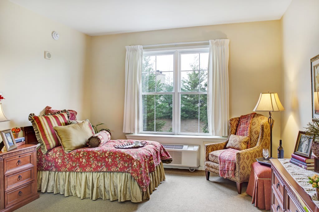 A cozy bedroom with a bed and chair by a large window, decorated in warm tones.