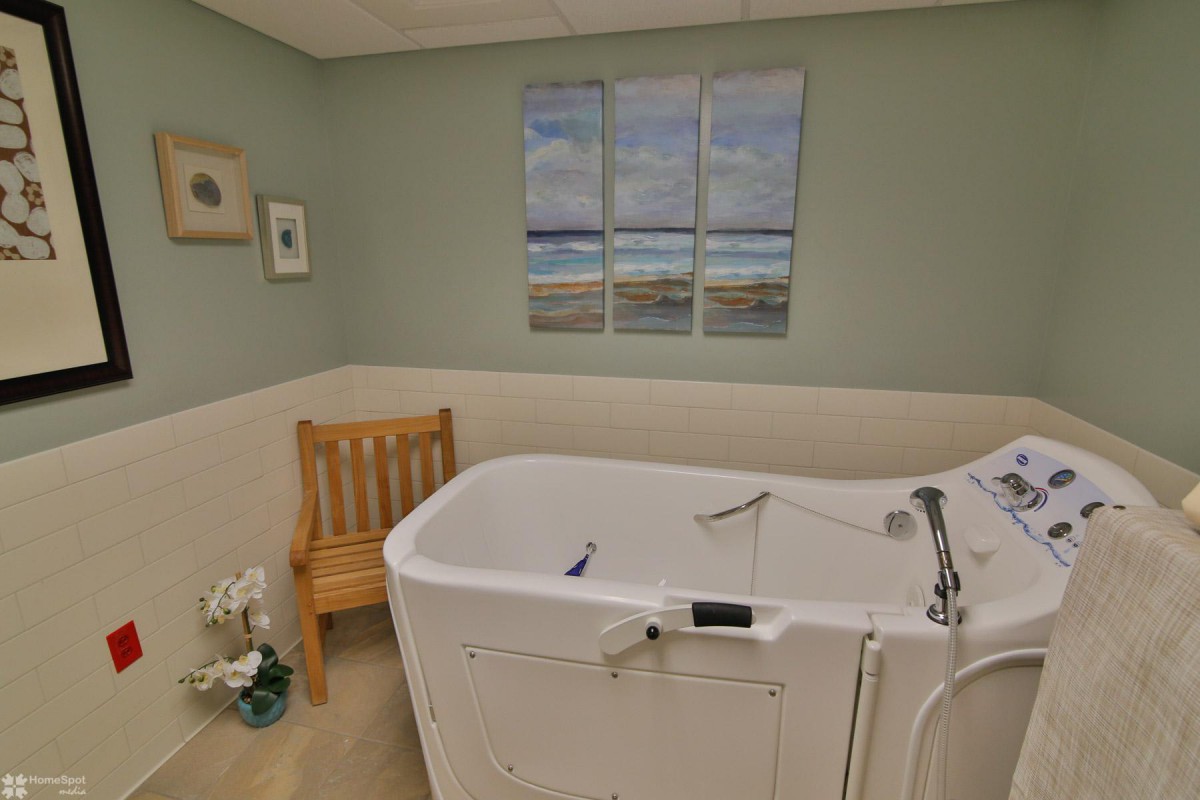 A bathroom featuring a walk-in bathtub, wooden chair, and seaside artwork on the wall.