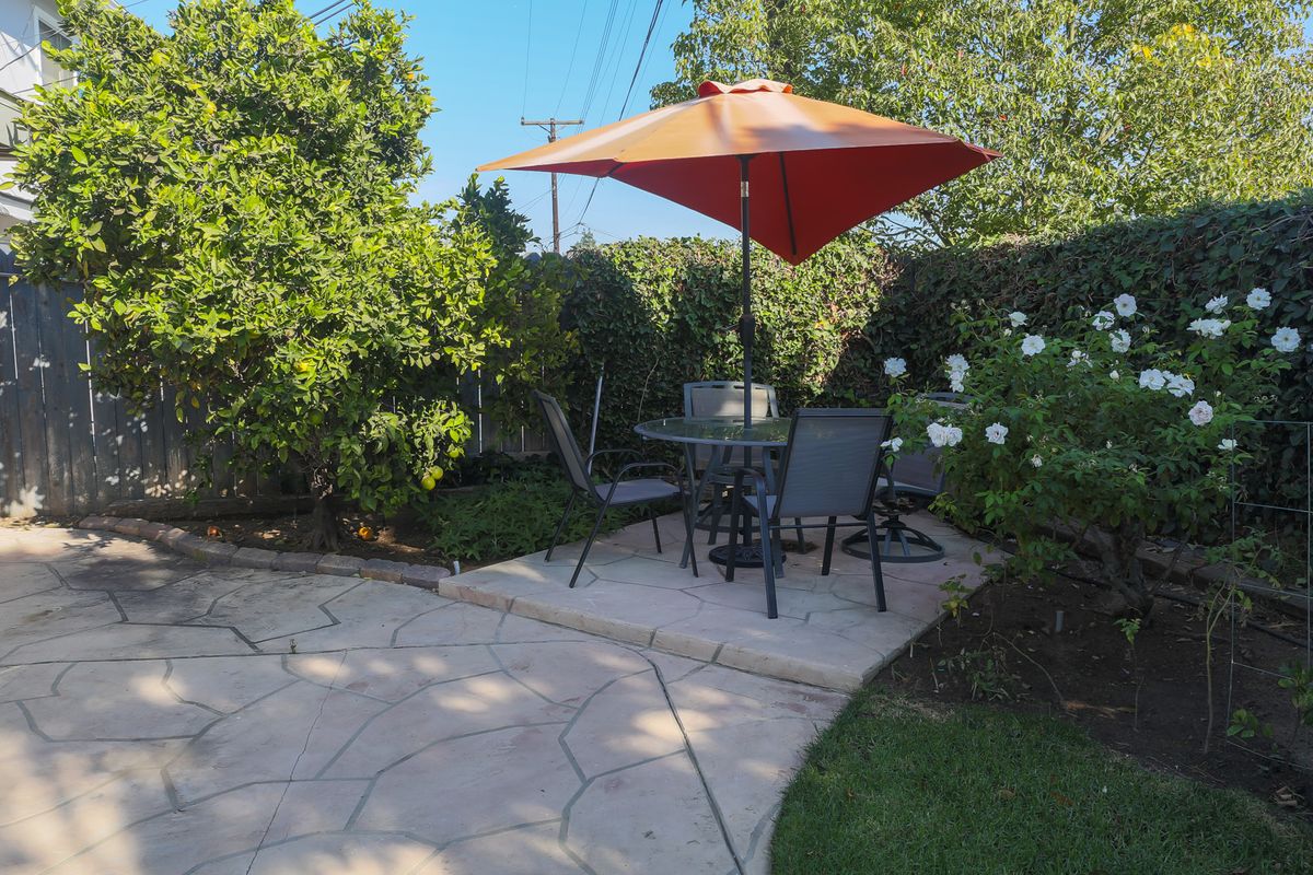 A sunny garden patio with chairs, a table, and an orange umbrella.