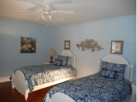 A bedroom with two twin beds featuring blue bedding, complemented by wall art and a ceiling fan.