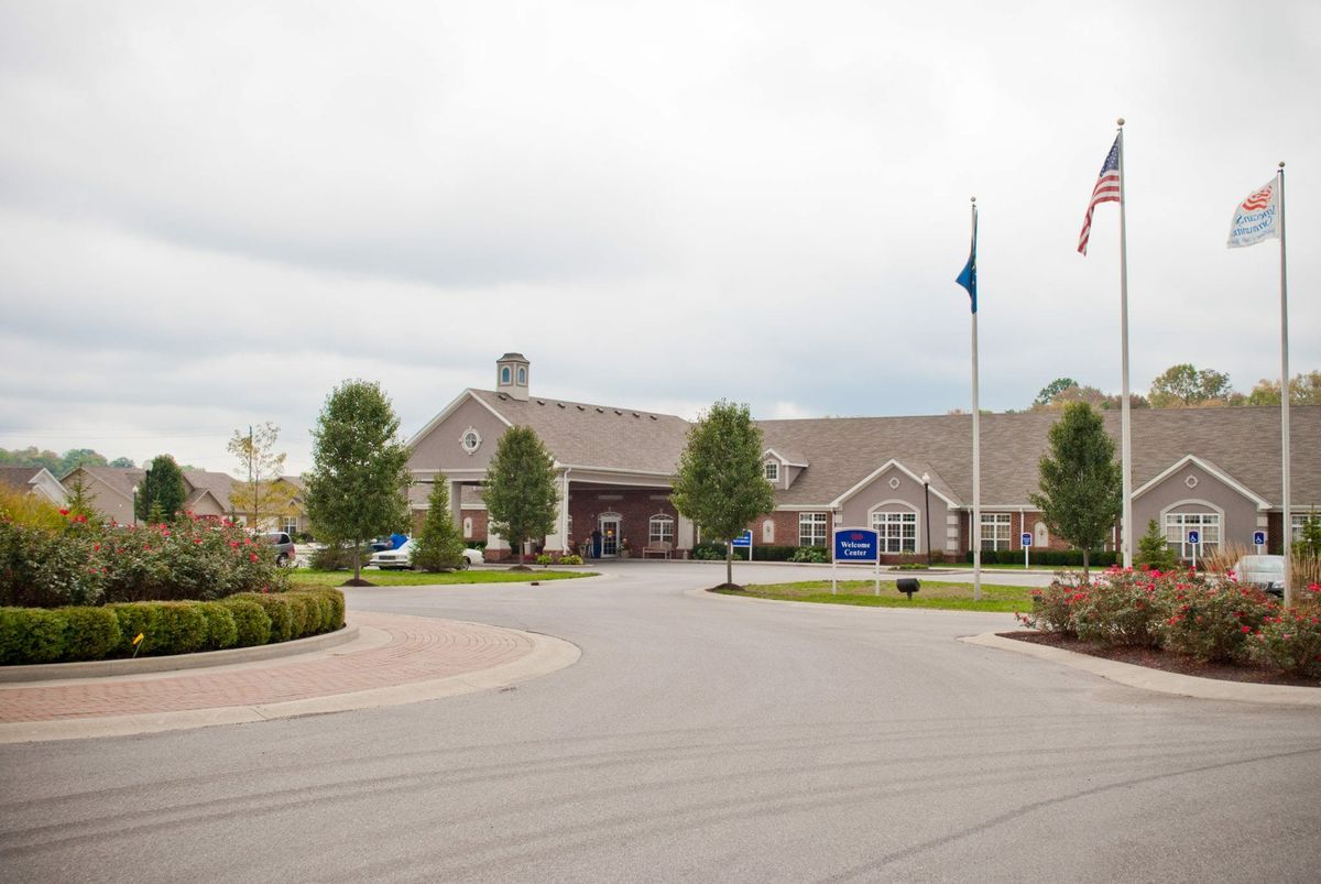 A spacious building with flags stands amidst a landscaped driveway under a cloudy sky.