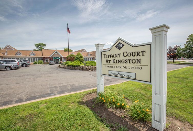 A sign for 'Tibasy Court at Kingston Senior Living' in front of a residential building and landscaped driveway.