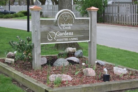 A wooden sign for 'Gardens' community housing, surrounded by decorative landscaping.