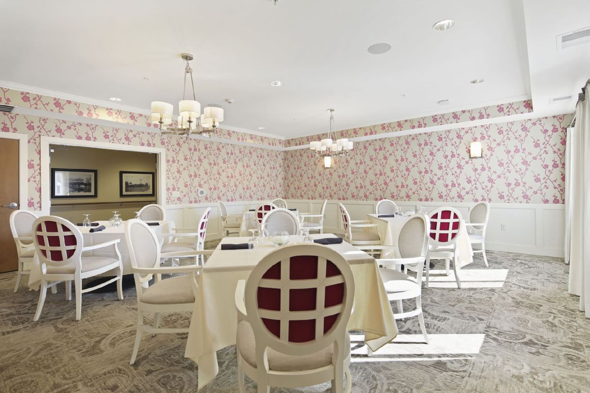 An elegant dining room with white chairs and tables, decorated with patterned wallpaper and chandeliers.