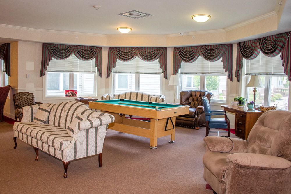 A cozy living room with a pool table, sofas, and large windows adorned with curtains.