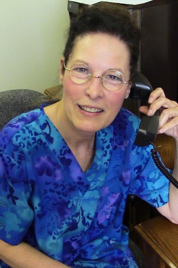 A person wearing glasses and a blue shirt is smiling while talking on the phone in an office setting.