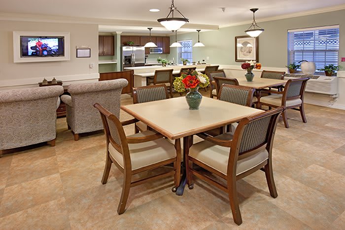 A cozy dining area with a table set and chairs, featuring warm lighting and a view into the kitchen.