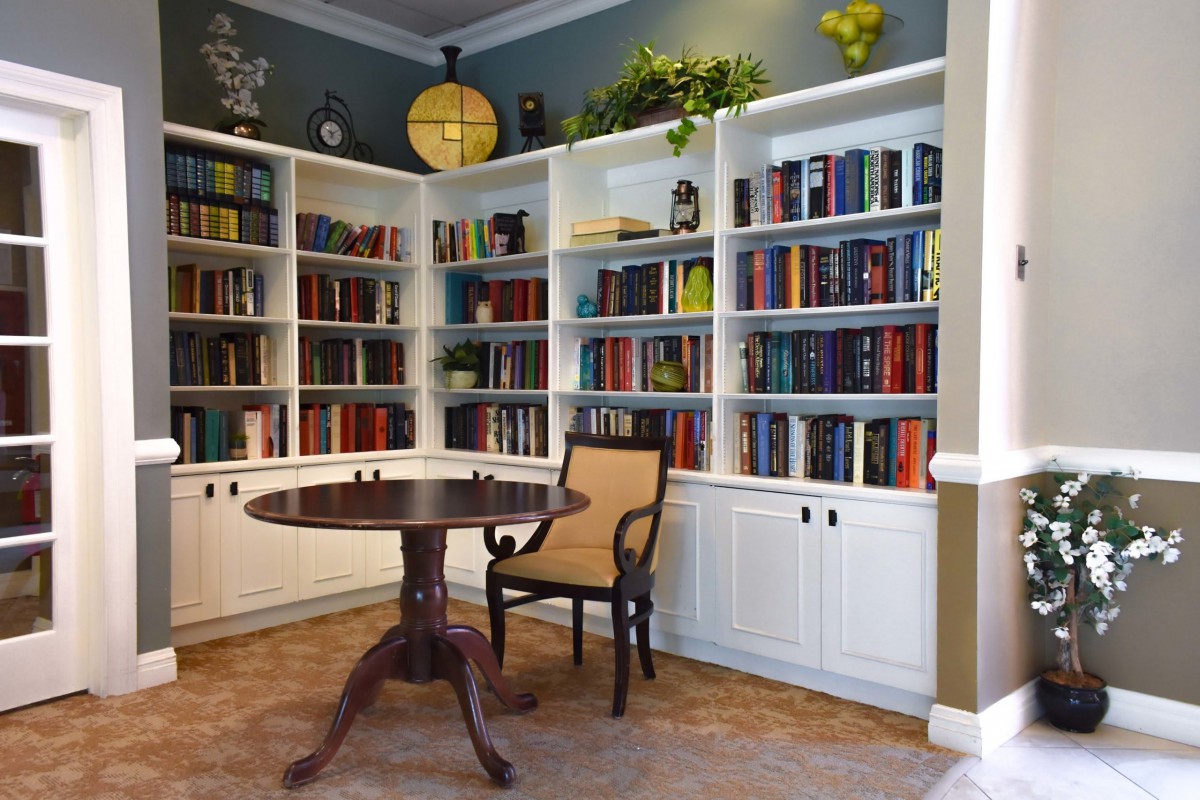 A cozy library corner featuring a round table and chair surrounded by white bookshelves filled with books.