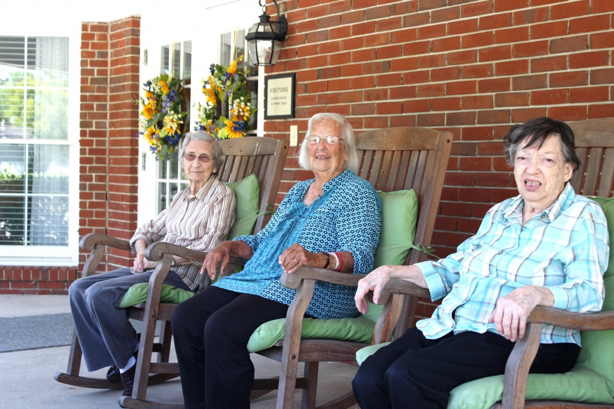 Three elderly women sitting on rocking chairs on a porch.