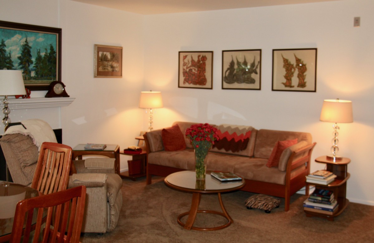 A cozy vintage-style living room featuring a sofa, armchair, coffee table, and decorative paintings on the wall.