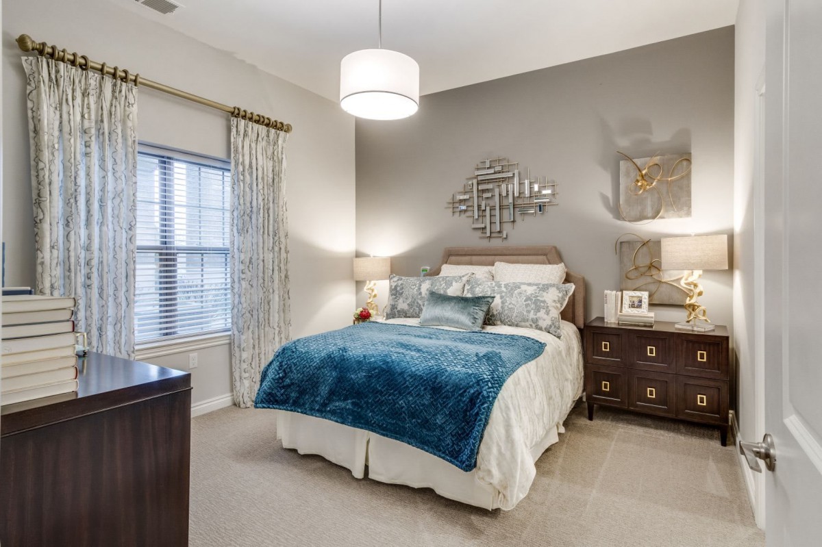 A modern bedroom interior featuring a cozy bed with blue accents, a decorative mirror on the wall, and stylish furniture.