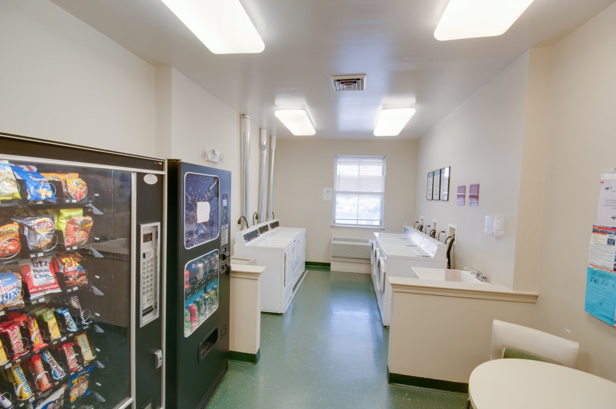 A clean and organized laundry room with washing machines, dryers, and a vending machine.