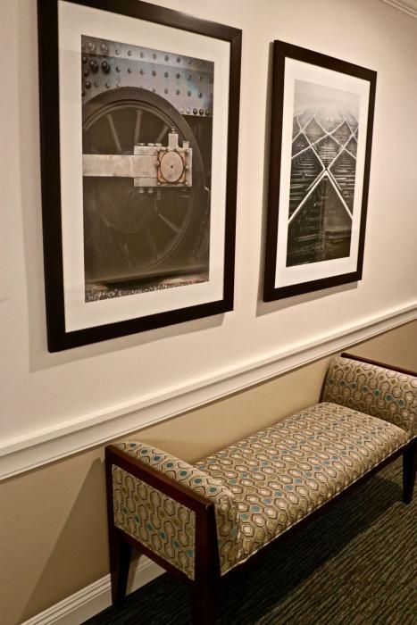 A hallway featuring a patterned bench and framed black-and-white photographs, one of a large gear and another of railroad tracks.