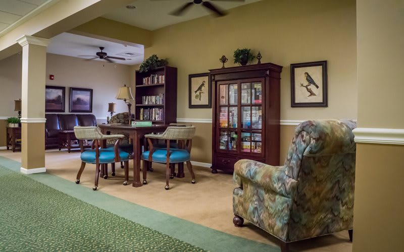 A cozy living room with a bookshelf, table, chairs, and an armchair.