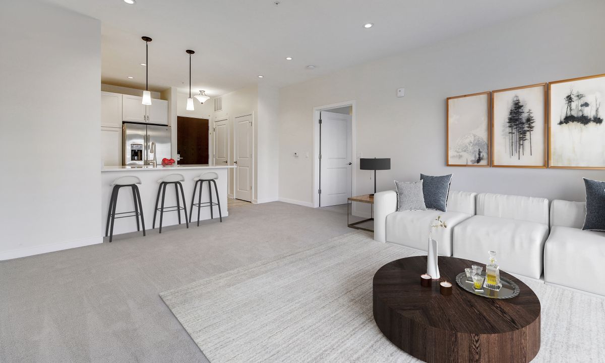 A modern open-plan living area featuring a minimalist design with a kitchen, bar stools, and a cozy sofa setting.