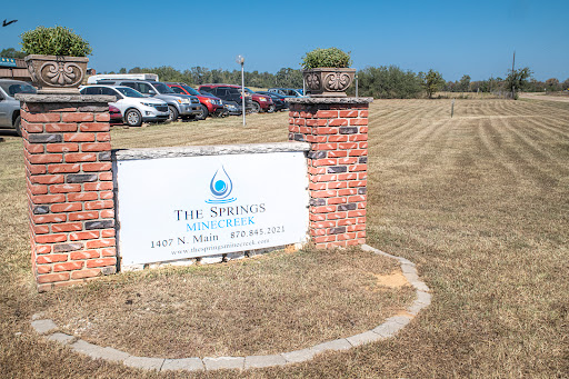 Entrance sign for The Springs, with a view of the parking area and open field.