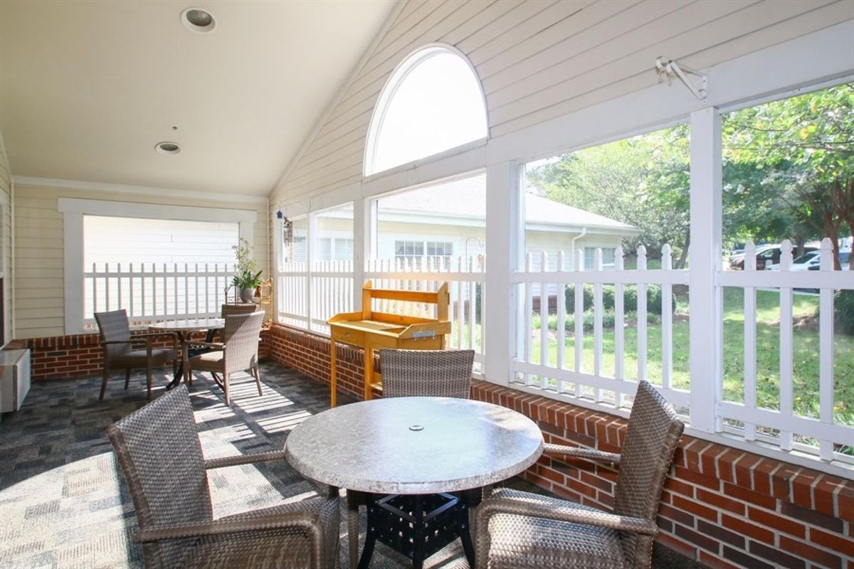 A bright patio area with outdoor seating, featuring a table and chairs surrounded by a white fence and brick walls.
