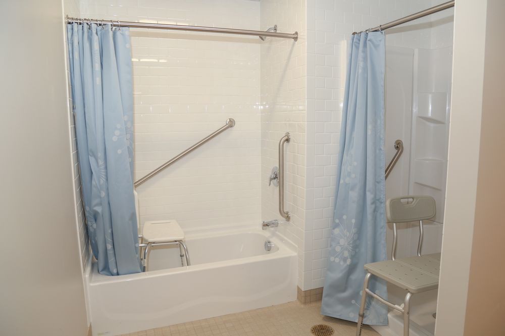 A bathroom with accessibility features including a shower chair and grab bars.