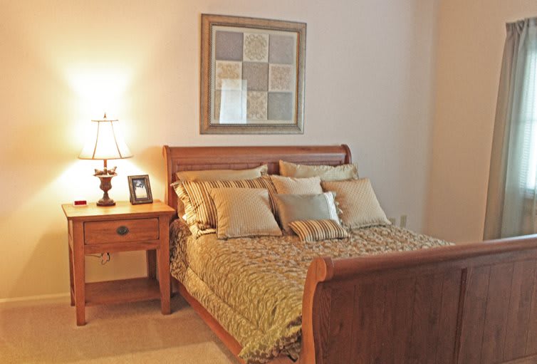 A cozy bedroom with a wooden bed and nightstand, accompanied by decorative pillows and a lamp.