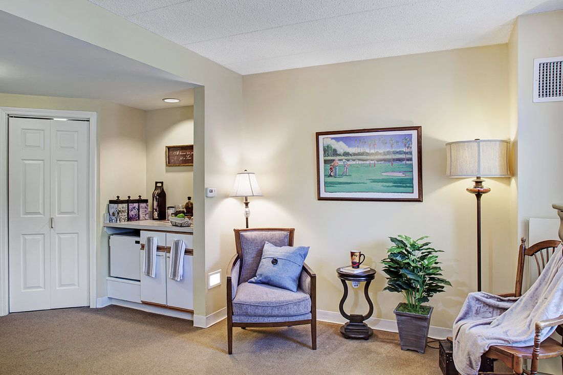 A cozy living area featuring a comfortable chair with a cushion, a side table with decorative items, and a potted plant under soft lighting.