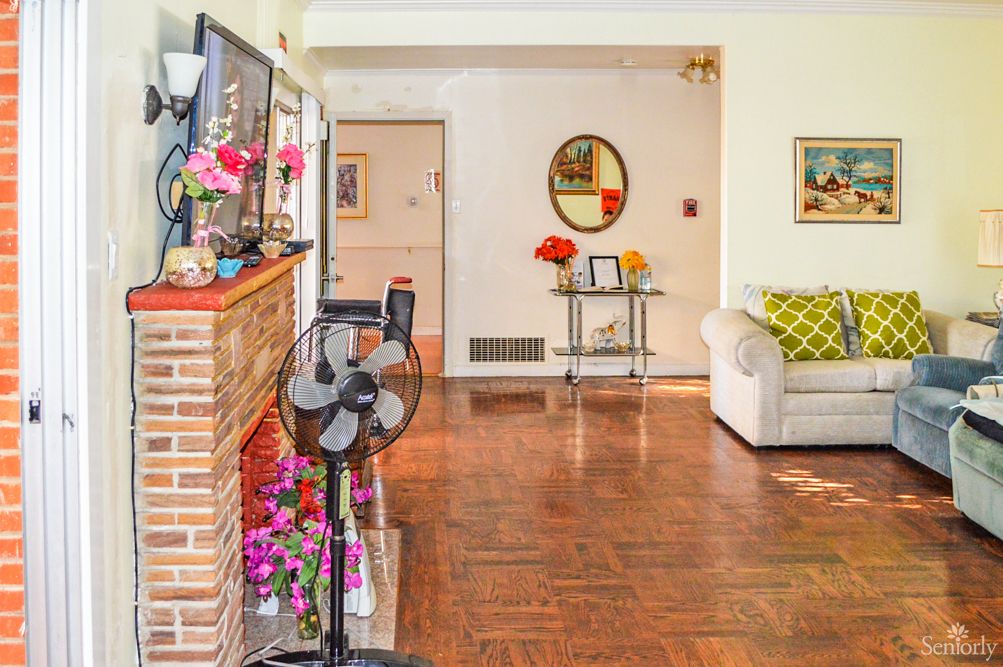 A cozy living room with wooden flooring, decorated with a mirror, flowers, and comfortable seating.