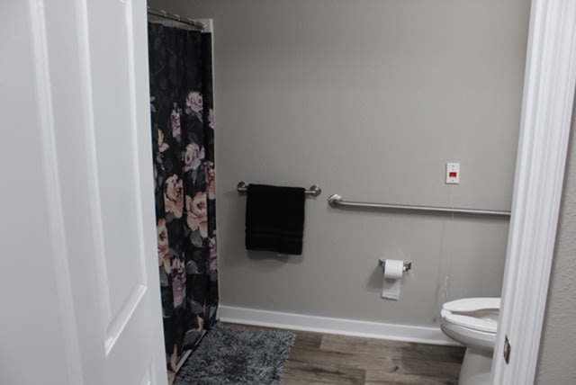 A modern bathroom with a floral shower curtain, toilet, and black towel on a rack.