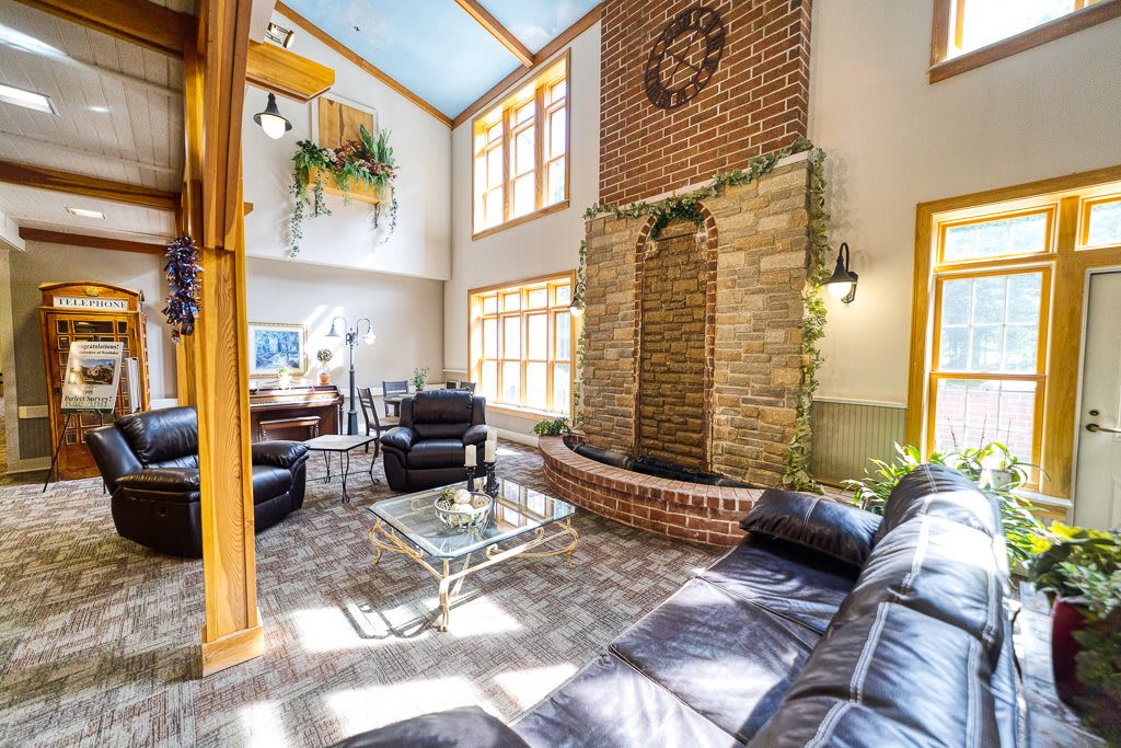 A spacious living room with abundant natural light, featuring leather sofas, a glass table, and a decorative brick water feature.