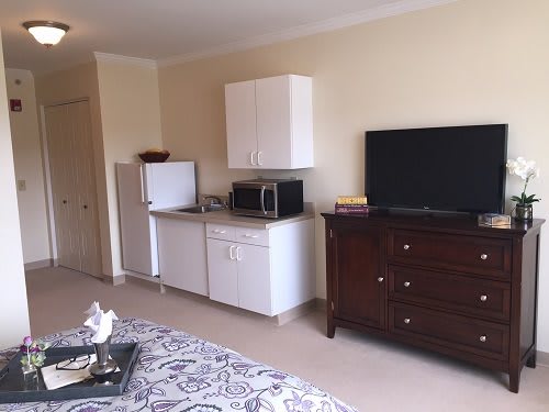 A cozy studio apartment featuring a kitchenette with appliances and a TV.
