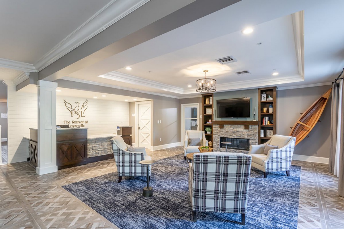 A spacious living room featuring modern decor with armchairs, a large blue carpet, built-in bookshelves, and a central fireplace.