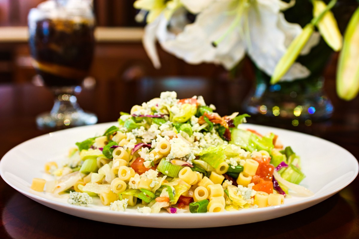 A colorful pasta salad with fresh vegetables and cheese on a white plate.