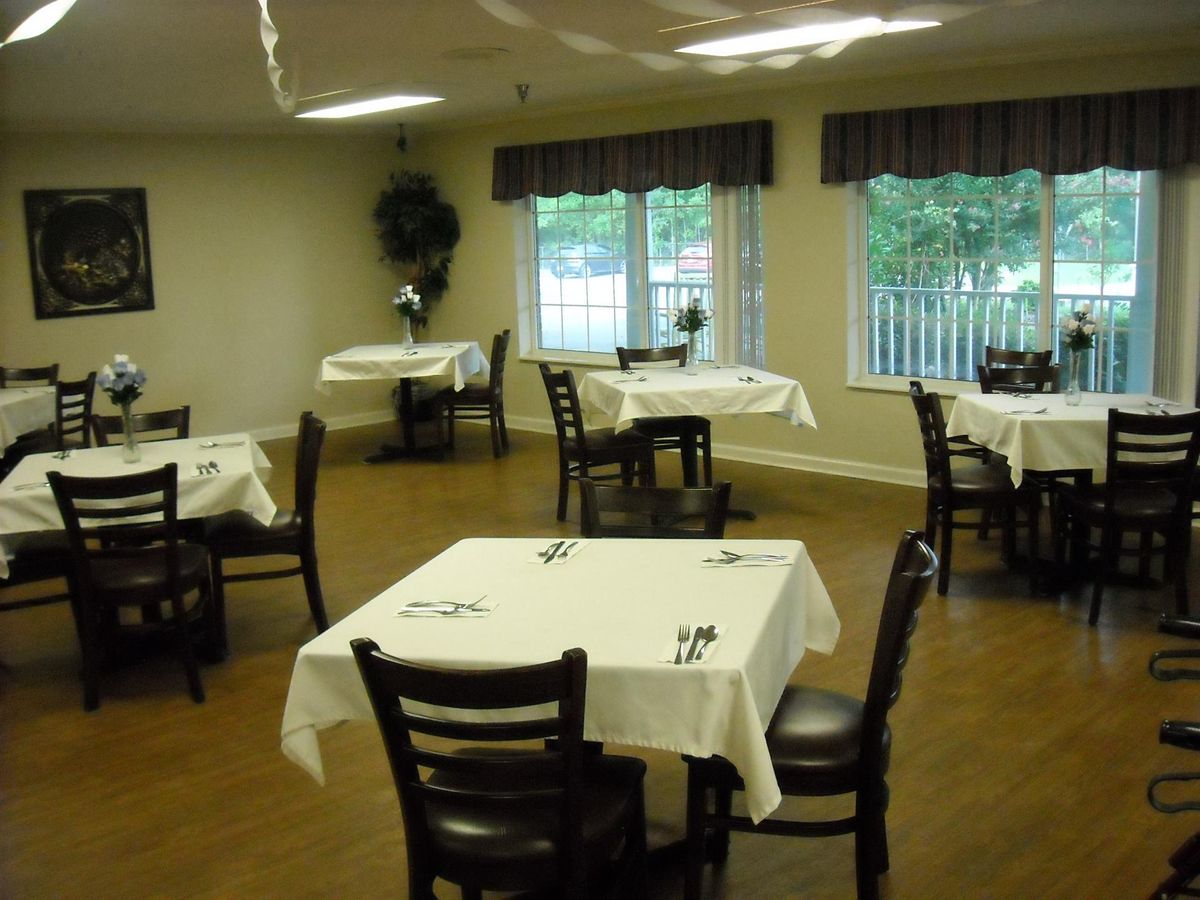 An empty dining room with neatly set tables and chairs, featuring windows with curtains.