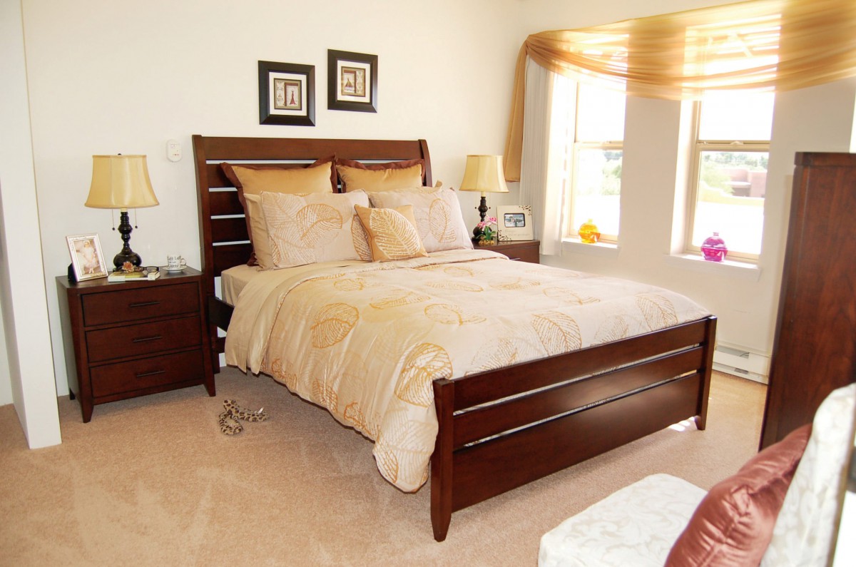 A cozy and well-decorated bedroom with a wooden bed, matching nightstands, and a sunlit window.